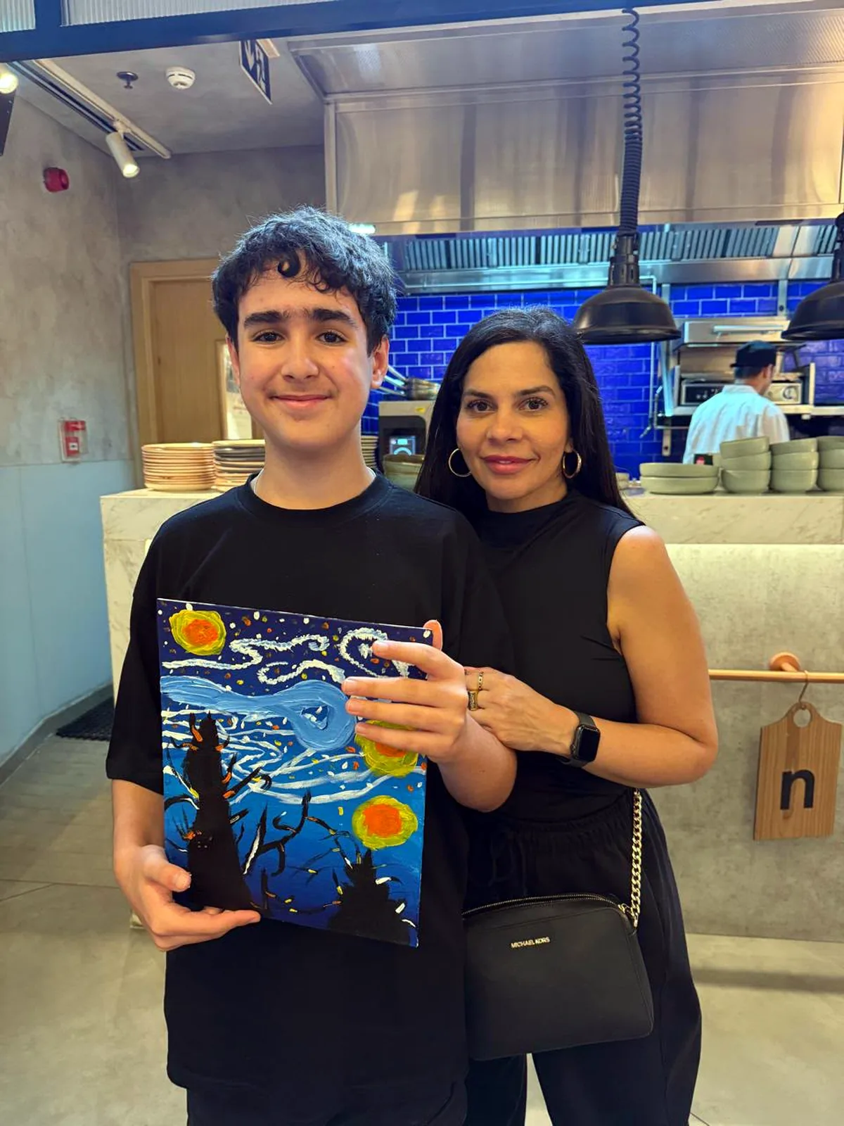 Mother and son holding their finished Starry Night canvases at a CANVAS painting session in a Dubai café